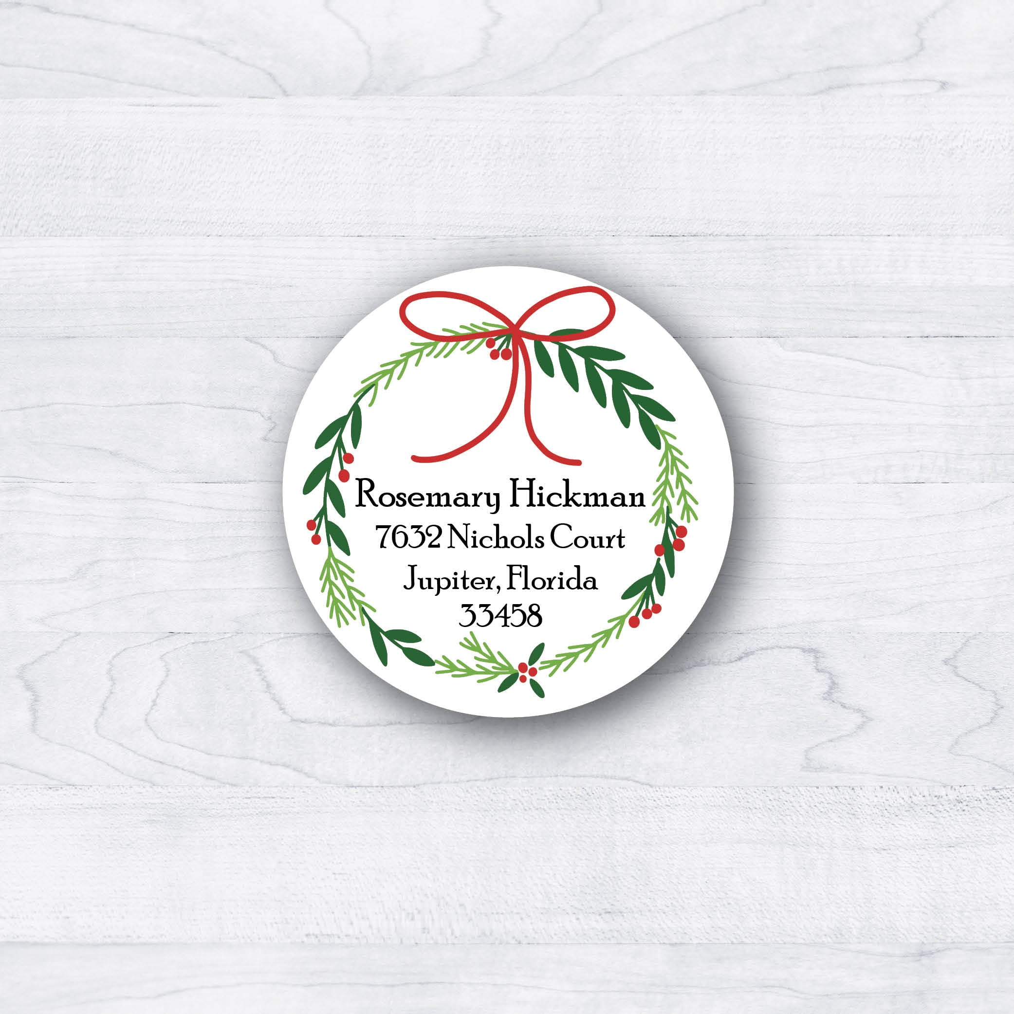 Green christmas wreath with red accents and a return address in the middle for the back of a christmas card