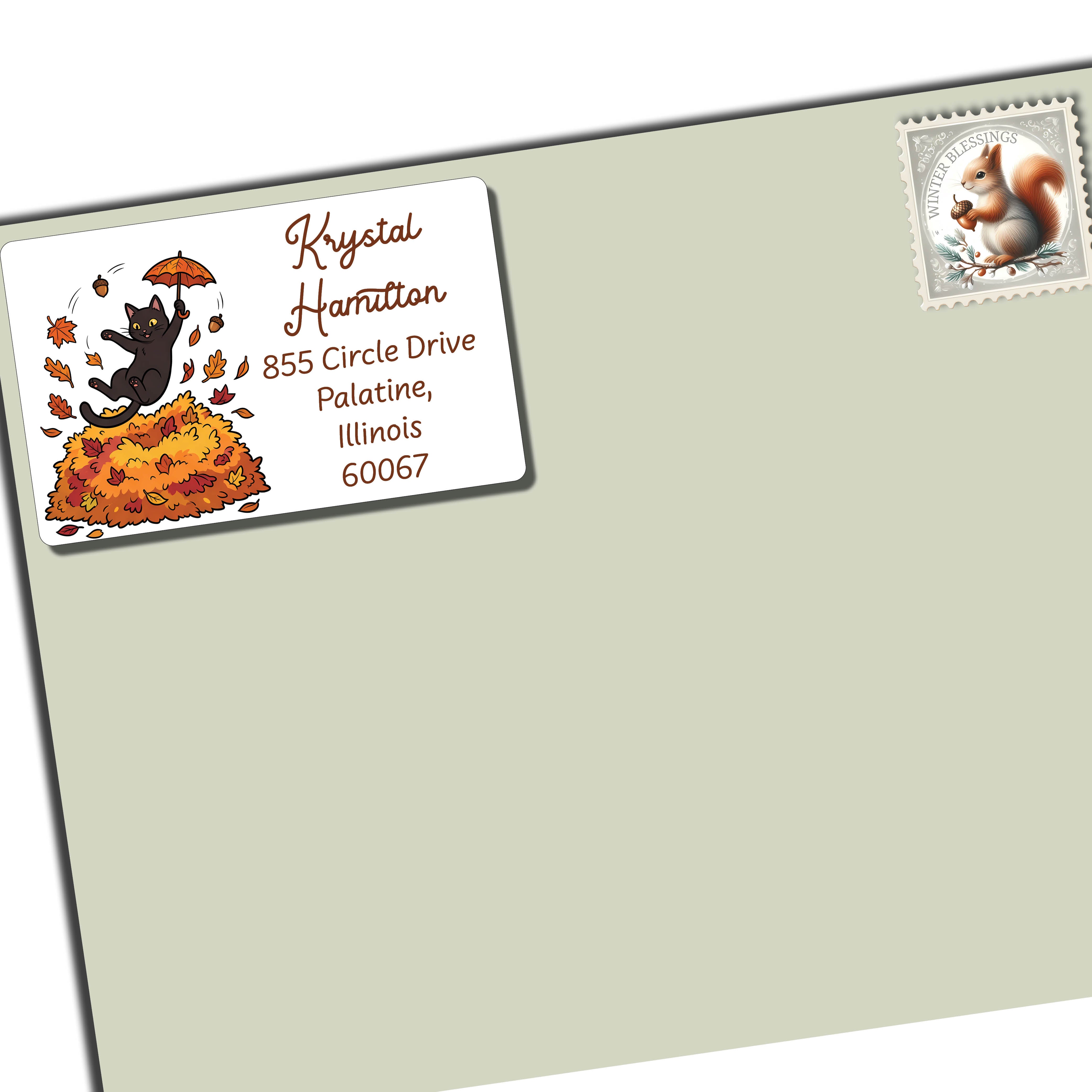 A light sage green envelope shown at an angle on a white background, with a sample address label in the upper left and a postage stamp in the upper right featuring a black kitten holding an umbrella.