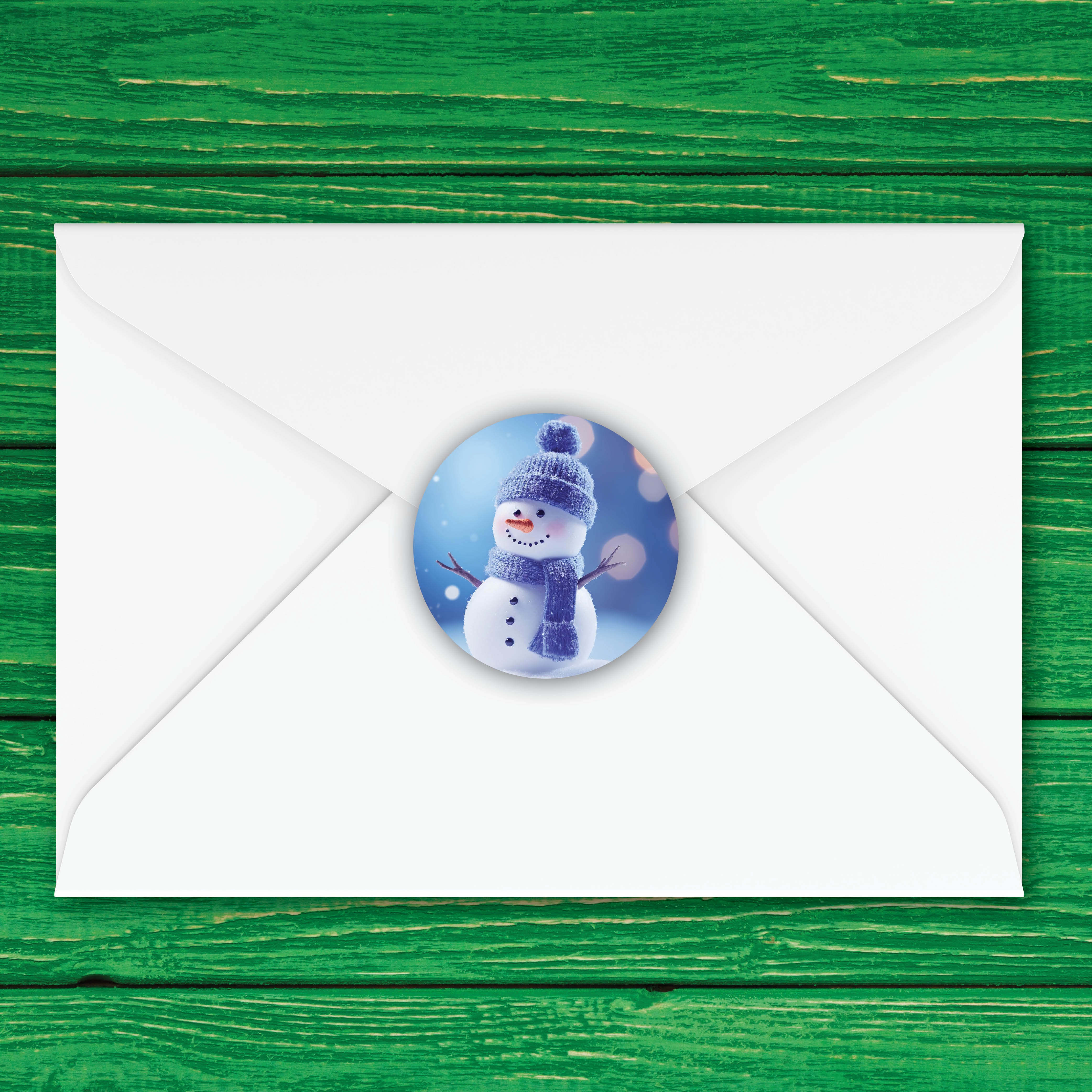 A white envelope centered on a green wooden background, with a round printed label on the center flap showing a smiling snowman in a blue hat and scarf against a snowy blue scene.