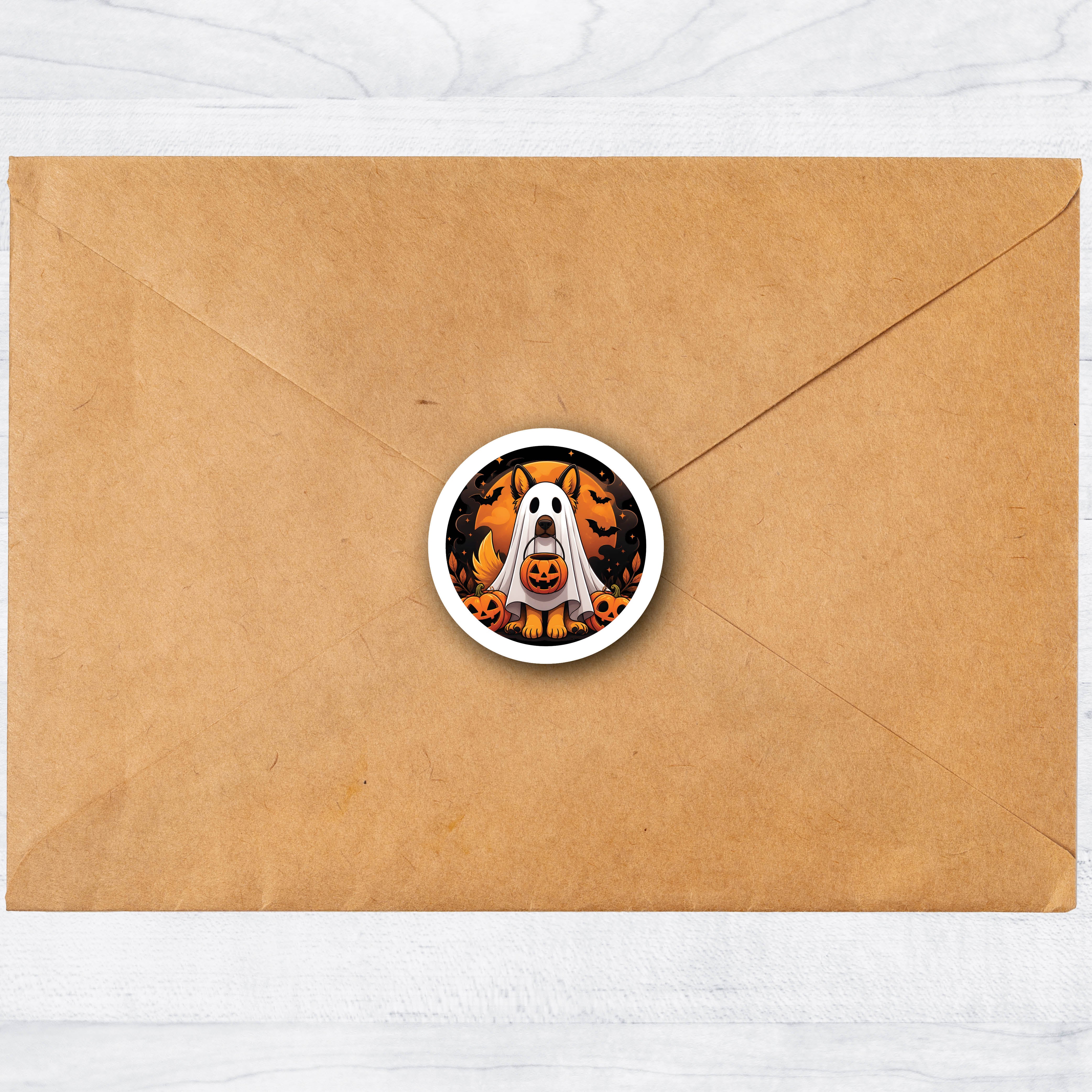 A round Halloween-themed label envelope seal featuring a white ghost and orange jack-o'-lanterns, centered on a brown kraft paper envelope against a light wood background.